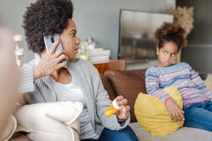 Portrait of an African American woman and her daughter at home, a mother is talking on the phone and holding pill bottle